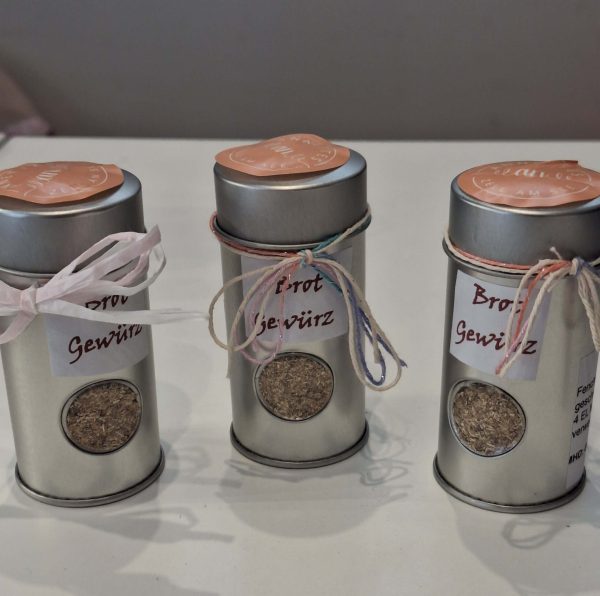 Drei Dosen Brotgewürz mit bunten Bändern und Etiketten auf einem weißen Tisch.