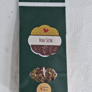 Kräutertee "Frau Sein" in grüner Verpackung, liebevoll handgemacht mit einem herzlichen Etikett.