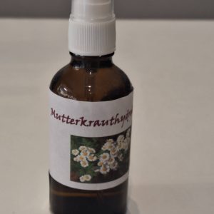 Braunglasflasche mit Sprühverschluss, beschriftet mit "Mutterkrauthydrolat" und Blumenmotiv.