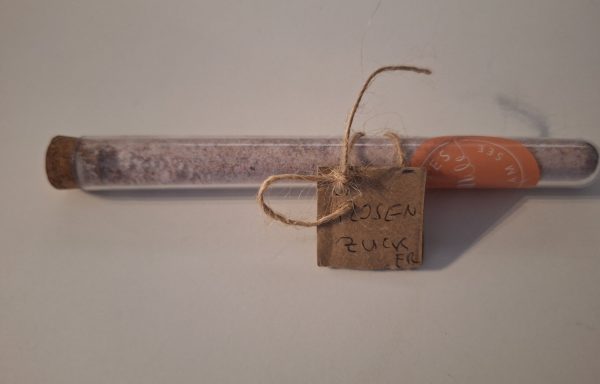 Röhrchen mit rosa Zucker, beschriftet mit „Rosen Zucker“ und dekoriert mit Schnur.