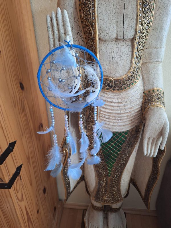Traumfänger in Blau mit Federn und Perlen, angebracht an einer Holzstatue.