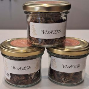 Drei Gläser mit Waldkräutern, beschriftet und in einem ansprechenden Design präsentiert.