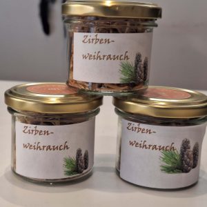 Drei Gläser mit Zirben-Weihrauch, dekoriert mit Etiketten und goldenen Deckeln.