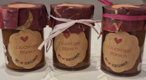 Drei Gläser mit fruchtigem Pfirsich, dekoriert mit farbigem Papier und Bändern.