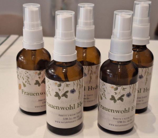 Fünf Flaschen Frauenwohl Hydrolat mit floralem Etikett auf einem Tisch.