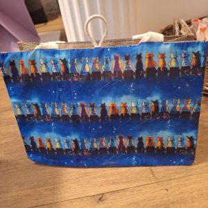 Tasche mit bunten Katzenmotiven auf blauem Hintergrund, ideal als kreative Geschenkidee.